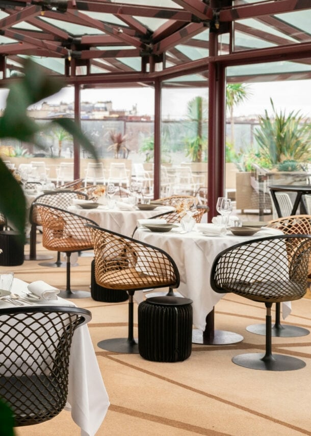 Interieur-Aufnahme eines modernen Restaurants mit gedeckten Tischen und bodentiefen Fenstern, die den Blick auf Paris freigeben.