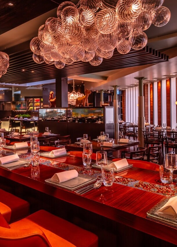 Opulent eingerichteter Speisesaal mit eingedeckter Holztafel und offener Küche.