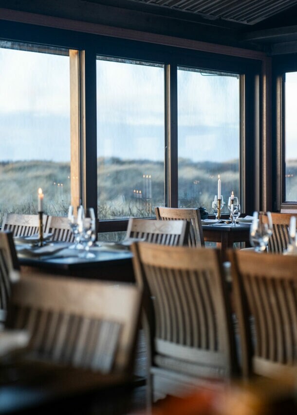 Gastraum der Sylter Sansibar, mit eleganten Tischen und Stühlen aus dunklem Holz und einem herrlichen Ausblick auf die umliegende Dünenlandschaft.