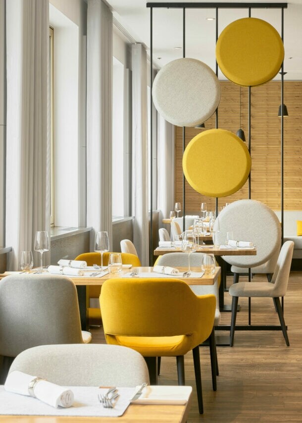 Helles stilvolles Interieur mit gelben und cremefarbenen Sitzmöbeln, dekorativer Trennwand und holzverkleideten Wänden.