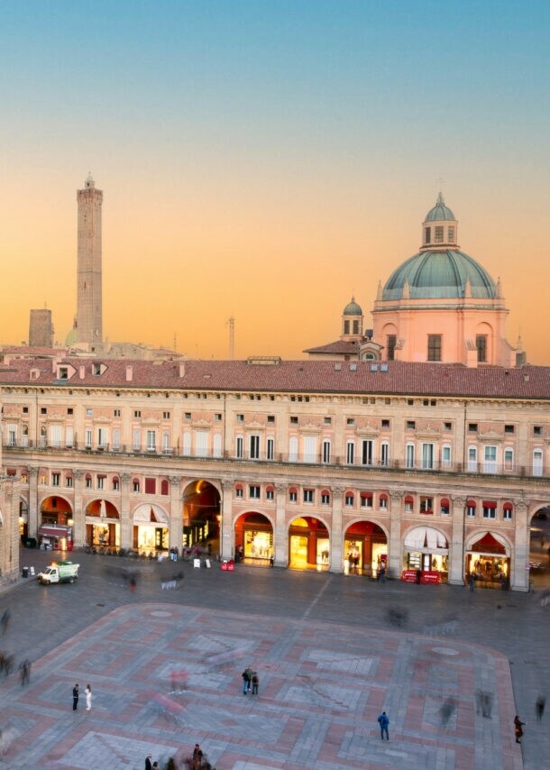 Historische Gebäude mit Arkaden und Turm am Piazza Maggiore in Bologna bei Sonnenuntergang
