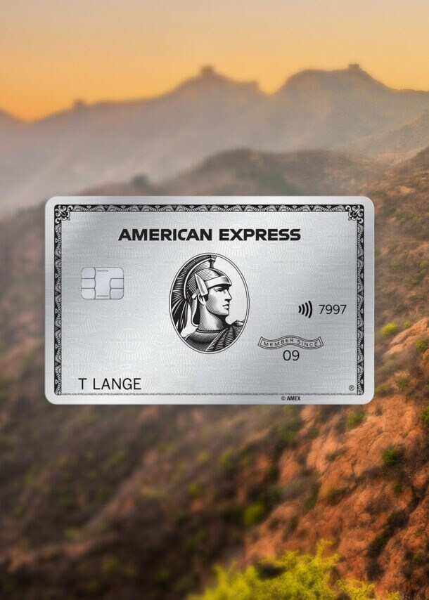 Abschnitt der Chinesischen Mauer mit Wachturm in Berglandschaft bei Sonnenuntergang, im Vordergrund eine silberne Platinum Kreditkarte von American Express als Freisteller.