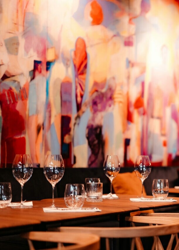 Mehrere eingedeckte Holztische vor einem bunten, großflächigem Wandbild.