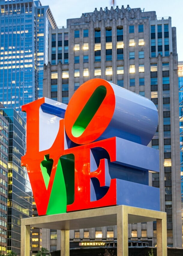 Skulptur mit dem Schriftzug 'LOVE' in roten und grünen Buchstaben vor Hochhäusern in einer Stadt