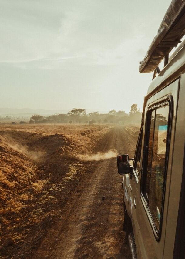 Safari-Fahrzeug fährt auf staubiger Piste durch afrikanische Savanne mit Zebras am Rand