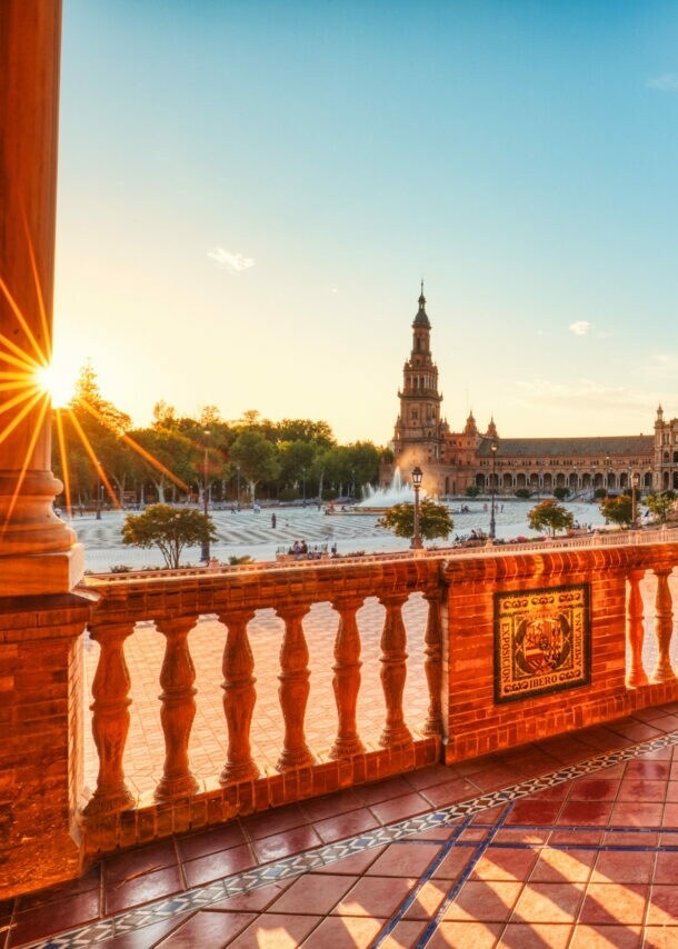 Überdachte Promenade an einem halbkreisförmigen Palastkomplex im andalusischen Stil an einem großen Platz im warmen Licht bei Sonnenuntergang.