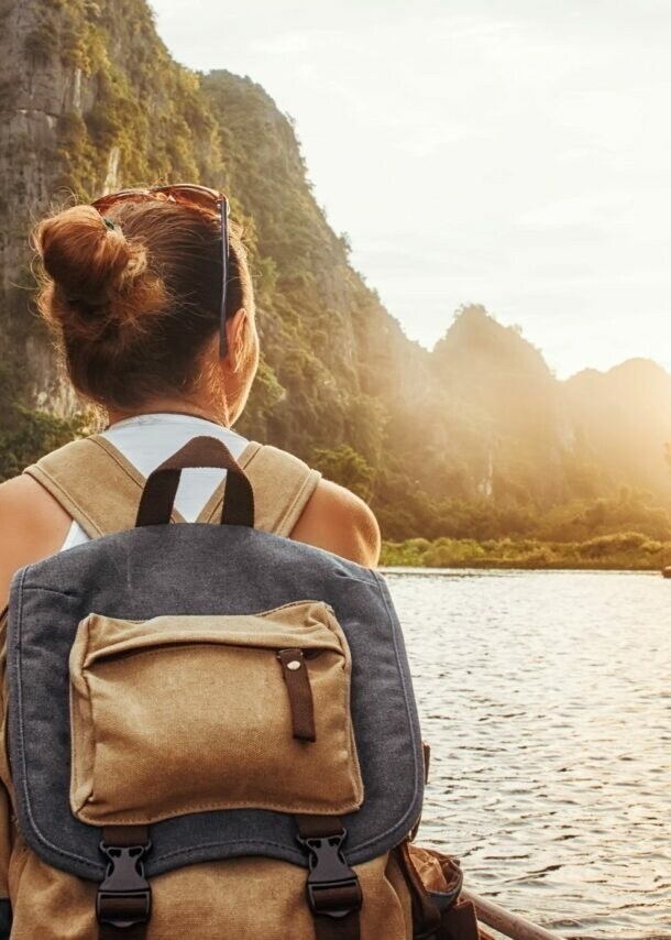 Frau mit Rucksack sitzt in einem Kanu auf einem Fluss, umgeben von hohen Felsen bei Sonnenuntergang.