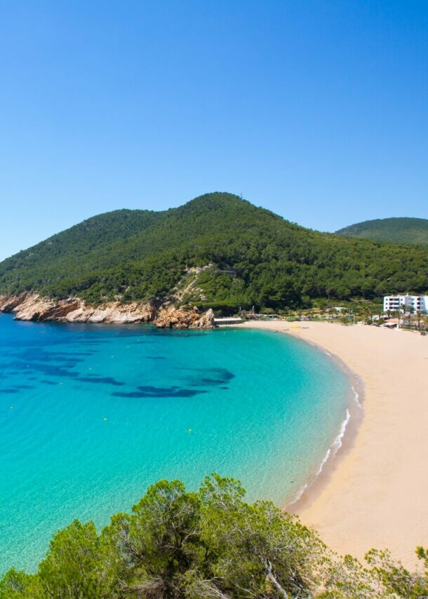 Bucht mit türkisfarbenem Wasser, Sandstrand und bewaldeten Hügeln unter klarem Himmel