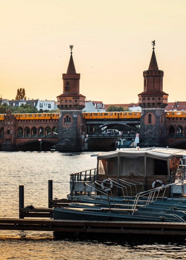Sonnenuntergang über der Oberbaumbrücke in Berlin mit vorbeifahrender U-Bahn und Booten auf der Spree.
