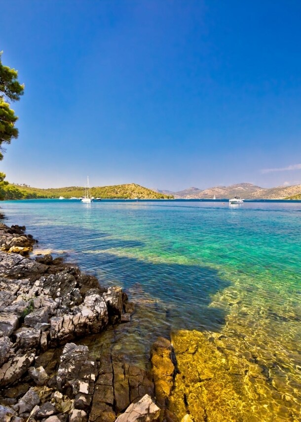 Bucht mit klarem Wasser und Booten umgeben von einer felsigen Landschaft mit Bäumen.
