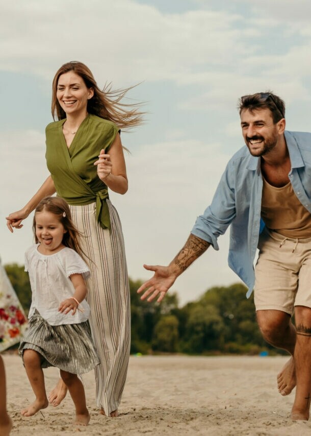 Familie mit zwei Kindern läuft barfuß am Strand bei bewölktem Himmel