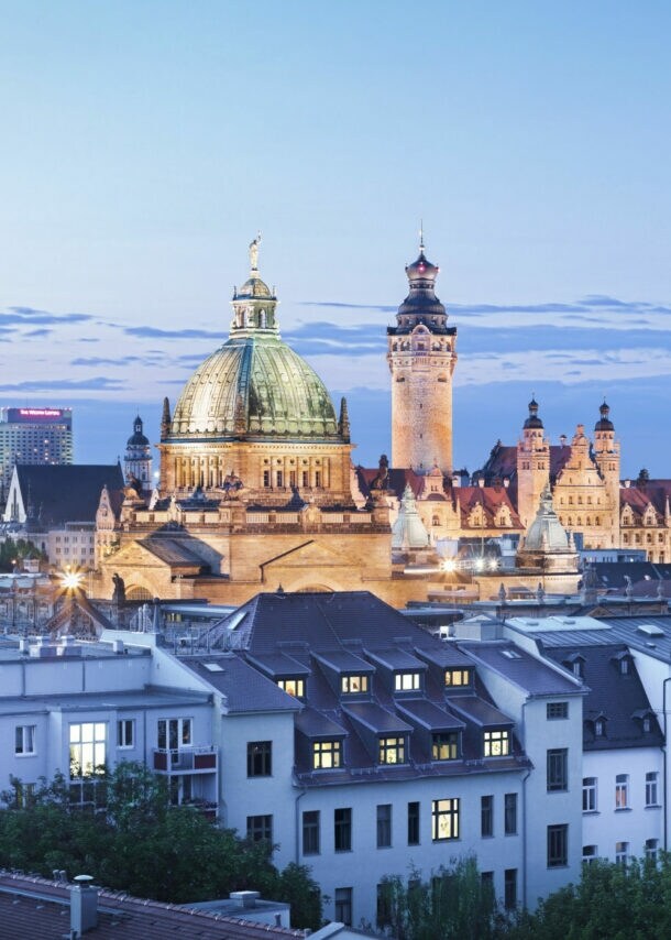 Skyline von Leipzig bei Abenddämmerung mit markanter Kuppel der Nikolaikirche und dem City-Hochhaus im Hintergrund