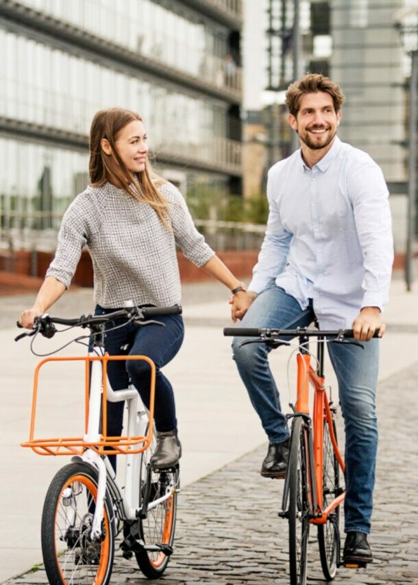 Paar hält Händchen beim Fahrradfahren auf einem gepflasterten Weg in einem modernen Stadtviertel