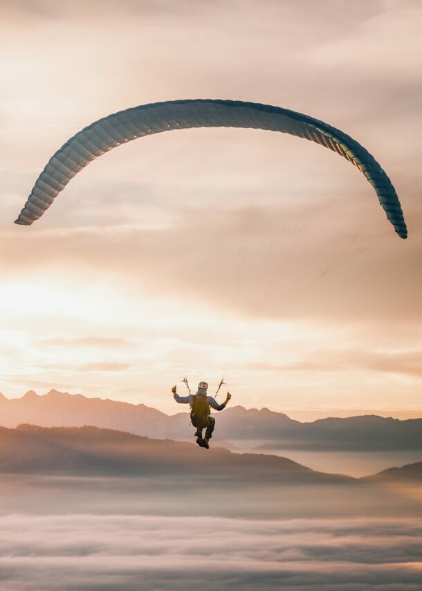 Person beim Gleitschirmfliegen über neblige Berglandschaft bei Sonnenaufgang