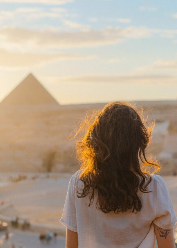 Frau mit lockigem Haar blickt auf die Pyramiden von Gizeh bei Sonnenuntergang