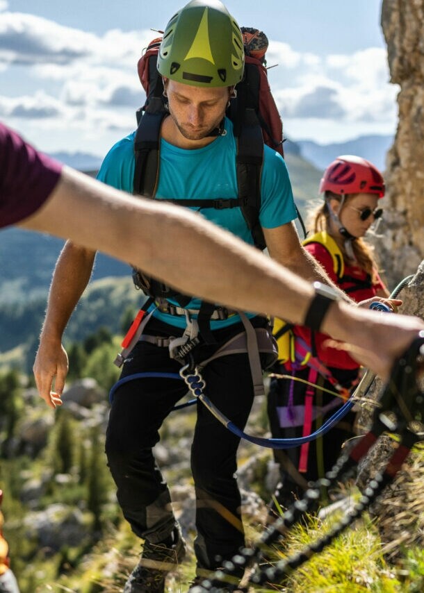 Drei Personen in Kletterausrüstung an einem Felsen mit Drahtseil.