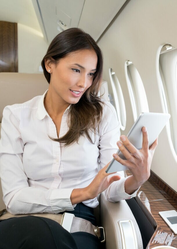 Eine Geschäftsfrau sitzt im Flugzeug und arbeitet an ihrem Tablet.