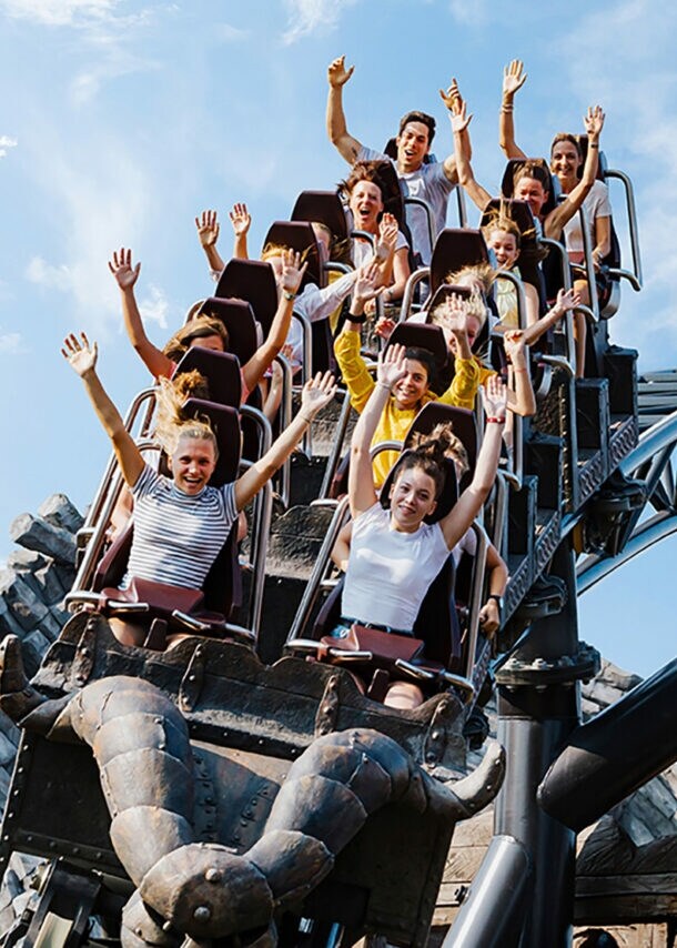 Menschen fahren auf der Achterbahn Taron im Phantasialand, Arme in die Luft gestreckt, vor blauem Himmel