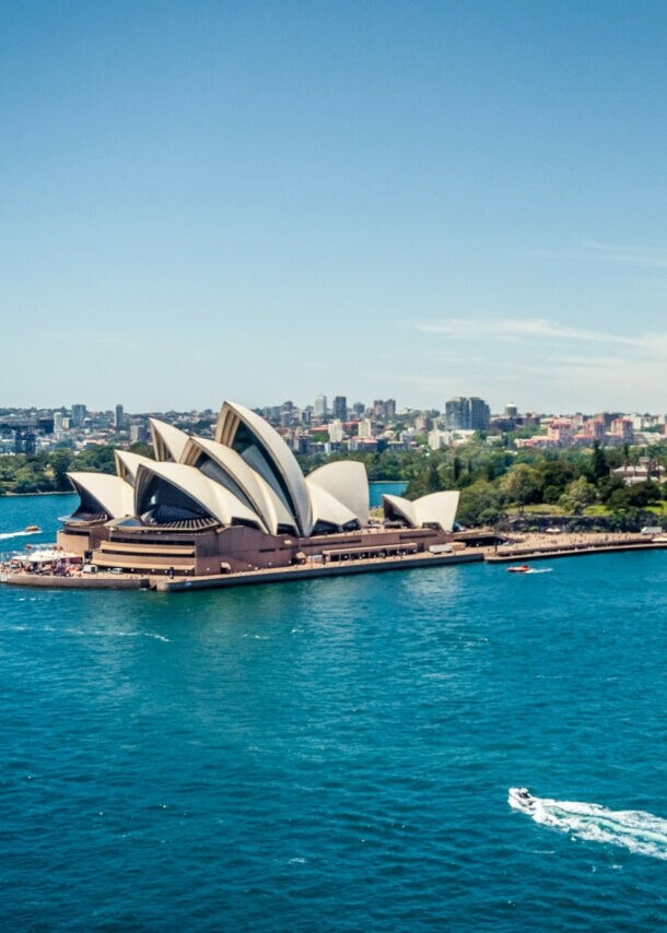 Sydney Opernhaus am Hafen mit Boot auf blauem Wasser und Hochhäusern im Hintergrund