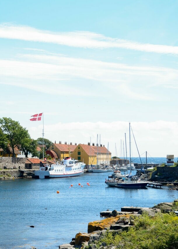 Hafen mit Segelbooten und Fähre, dänische Flagge weht, historische Festung und Häuser am Ufer auf Bornholm