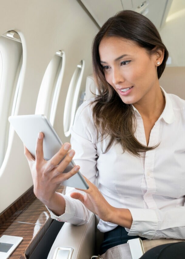 Geschäftsfrau sitzt auf einem Business-Platz im Flugzeug und blickt auf ein Tablet.