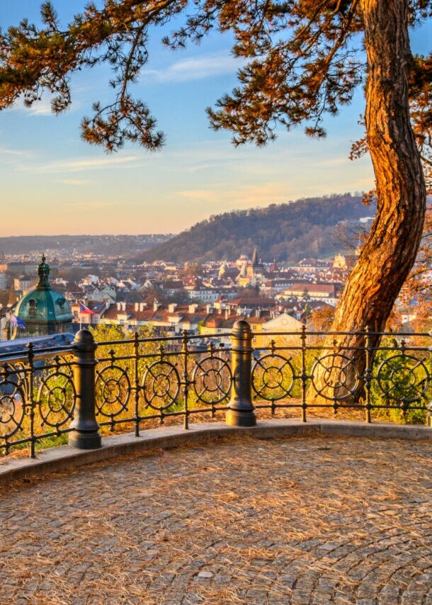 Blick auf die Moldau mit mehreren Brücken und der Altstadt von Prag im Sonnenuntergang, von einer Aussichtsplattform mit schmiedeeisernem Geländer