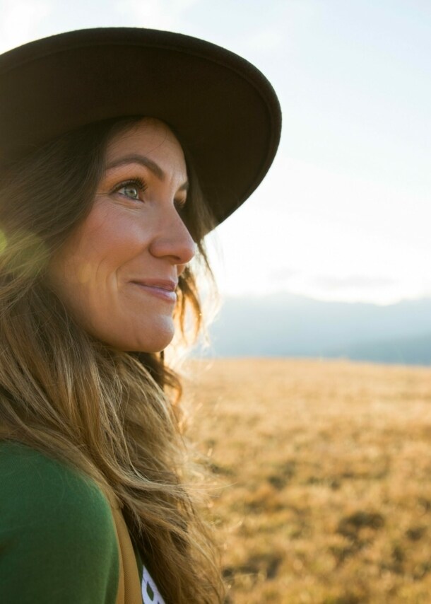Eine junge Frau mit Hut schaut auf einer Wanderung in die Ferne