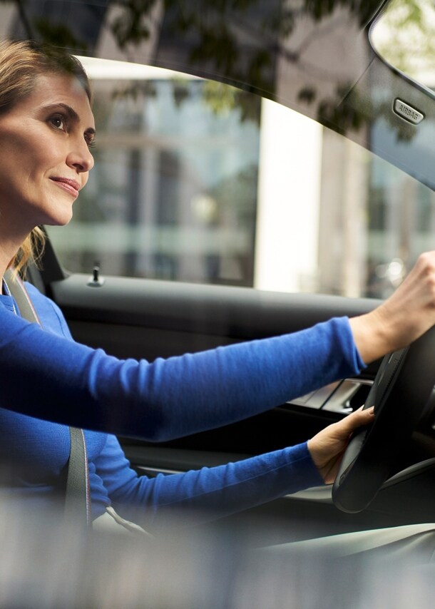 Eine Frau im blauen Pullover am Steuer eines BMW in urbaner Umgebung.