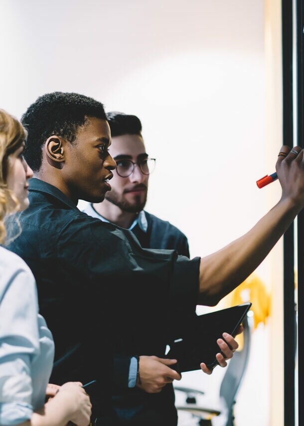 Eine Gruppe von Kolleg:innen steht am Whiteboard und erarbeitet in einem Workshop die Frage nach dem Warum.