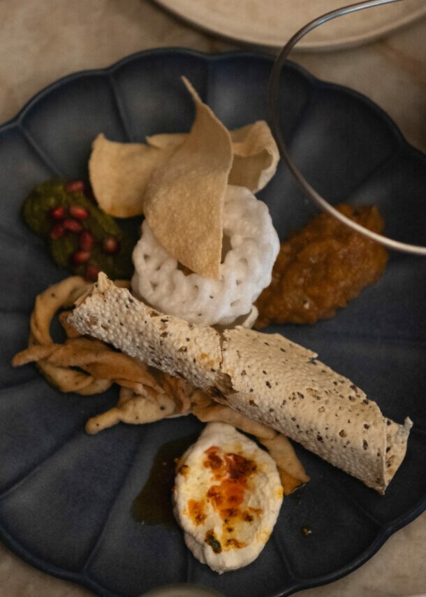 Ein blauer Teller mit verschiedenen indischen Gerichten: Reis in einer Schüssel, Papadam, Chutney, frittiertes Gemüse und ein gerolltes Fladenbrot.