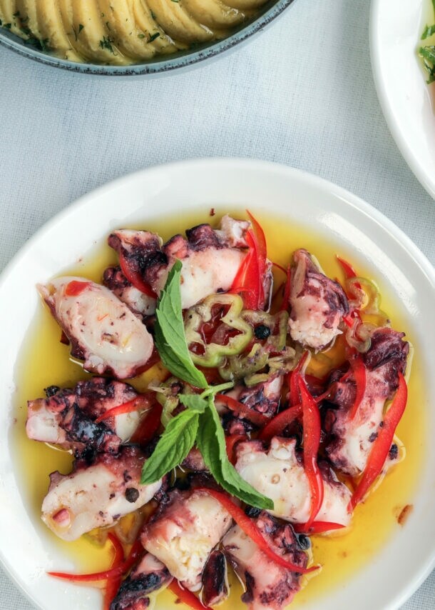 Verschiedene mediterrane Vorspeisen auf Tellern, darunter gegrillter Oktopus mit roten Paprikastreifen, Artischocken mit Tomatenscheiben und Kräutern, Gurkensalat und weitere Dips.