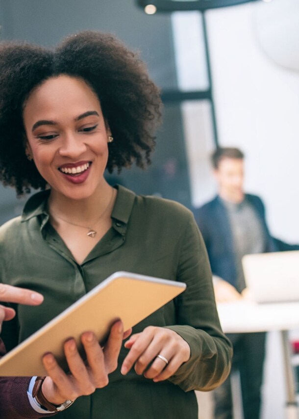 Zwei Kollegen stehen zusammen und schauen gemeinsam auf ein Tablet in einem Büro.