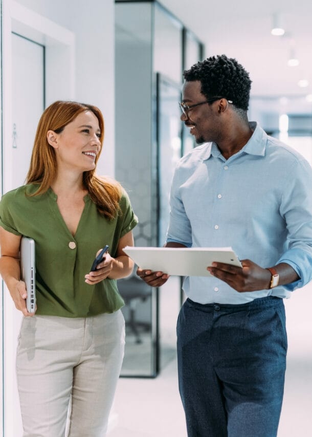 Eine Frau und ein Mann mit Tablets in den Händen kommunizieren auf einem hellen Flur.