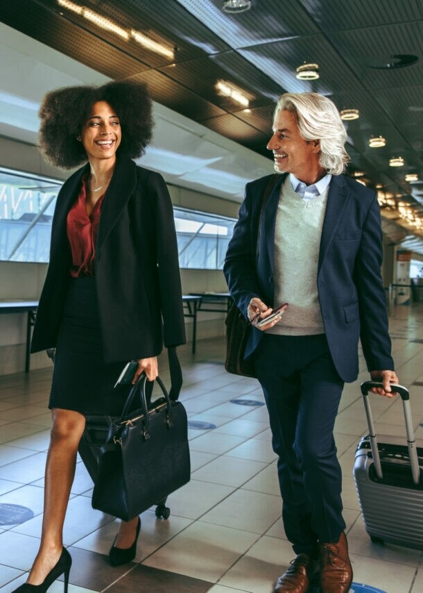 Drei Personen in eleganter Business-Kleidung mit Handgepäck laufen nebeneinander durch ein Flughafenterminal.
