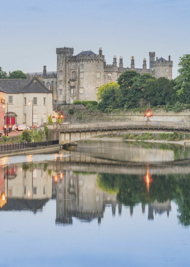 Blick auf Kilkenny mit Kilkenny Castle und der John’s Bridge vor dem Fluss Nore, indem sich die Lichter und Gebäude siegeln.