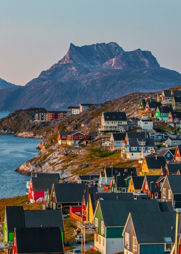 Bunte Häuser der grönländischen Hauptstadt Nuuk an einem Hang, der zum Wasser hin abfällt, im Hintergrund sind Berge.