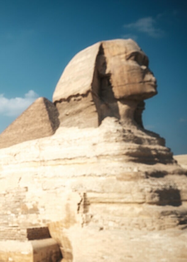 Eine Frau mit Hut fotografiert die Große Sphinx von Gizeh mit einem Smartphone bei klarem Himmel.