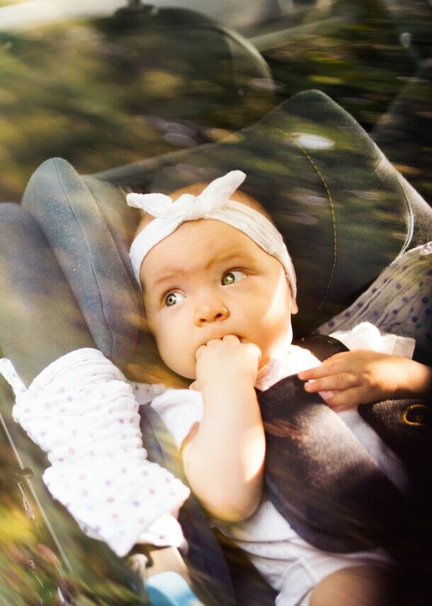 Kind sitzt auf dem Rücksitz eines Autos, hält ein Taschentuch und trägt eine weiße Bluse mit schwarzen Punkten.