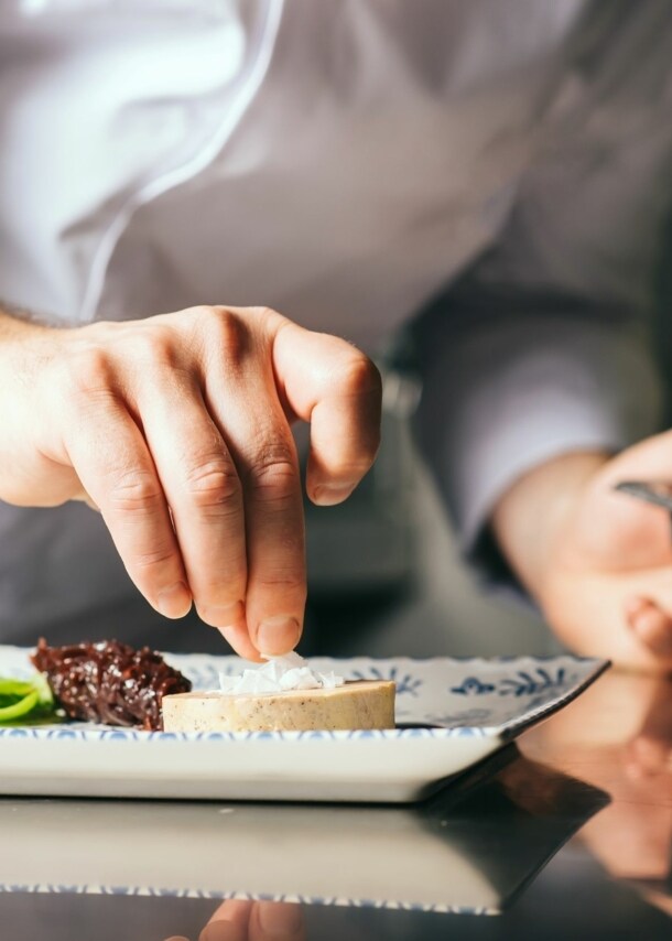 Hand eines Kochs, der einen Teller zubereitet.
