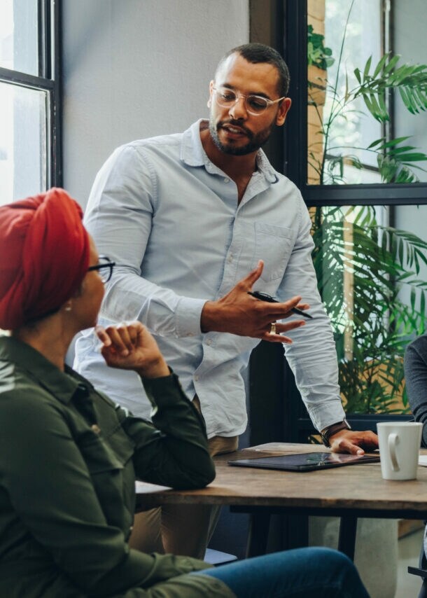 Mehrere Personen sitzen oder stehen an einem Tisch und schauen eine Person an, die spricht.