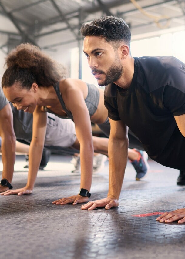 Mehrere Personen in Sportkleidung machen Liegestütze in einem hellen Fitnessstudio mit Gummiboden.