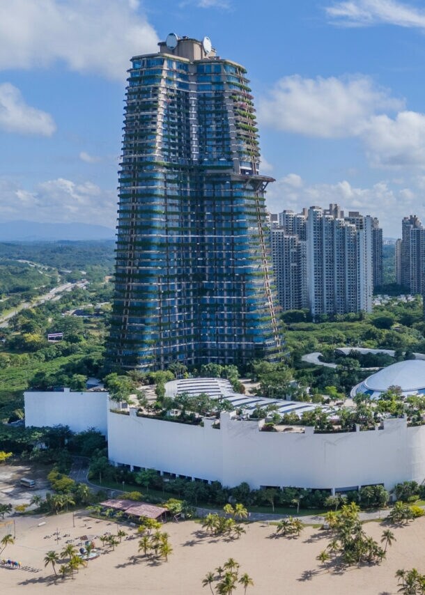 Blick auf eine moderne Küstenstadt in Ägypten mit hohem, runder Turm im Bau, mehreren Hochhäusern und einem Sandstrand am Meer.