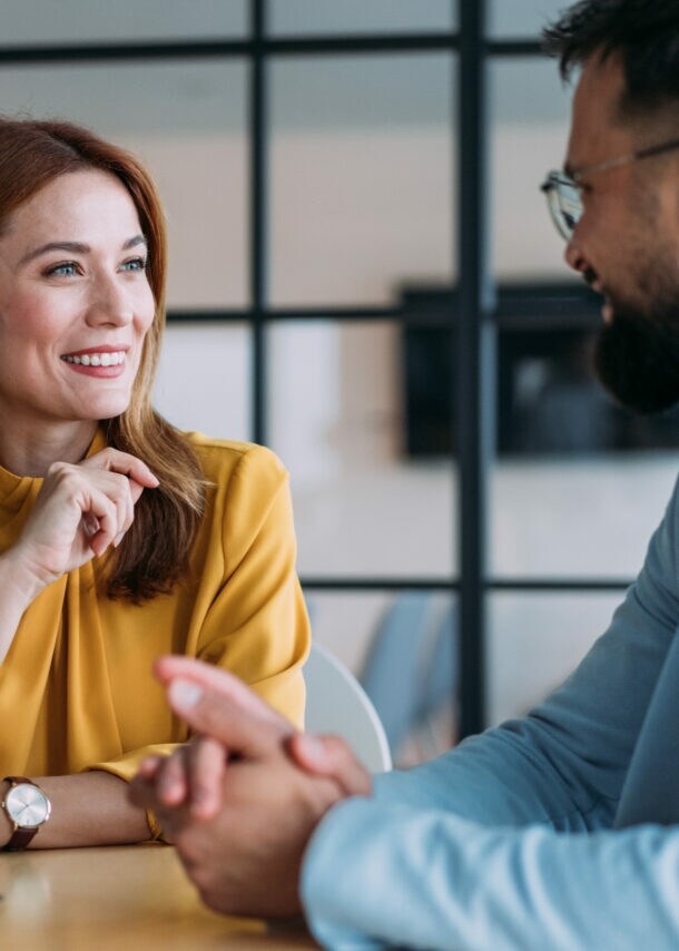 Eine Frau und ein Mann in eleganter Kleidung führen ein freundliches Gespräch an einem Tisch in einem Büro.