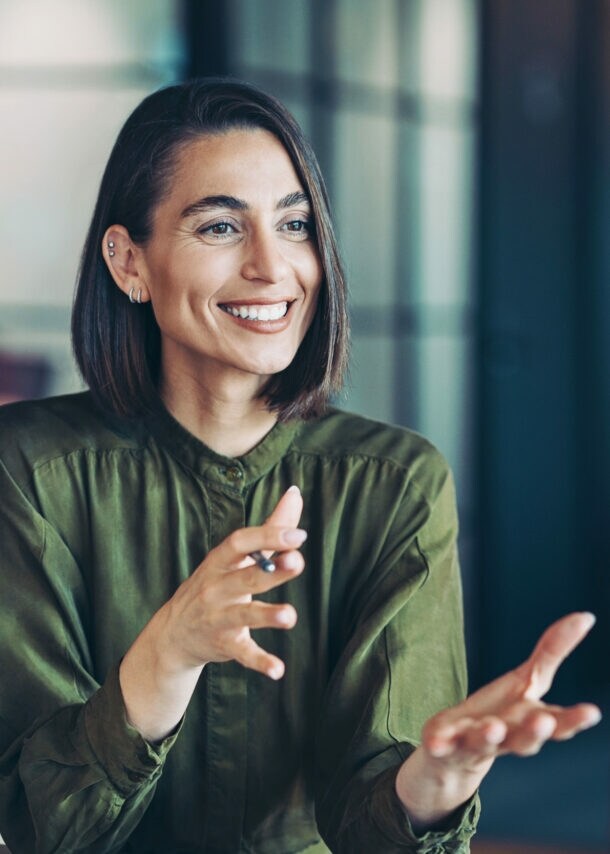 Eine lächelnde Frau in grüner Bluse im Gespräch mit einer nur von hinten erkennbaren Person.