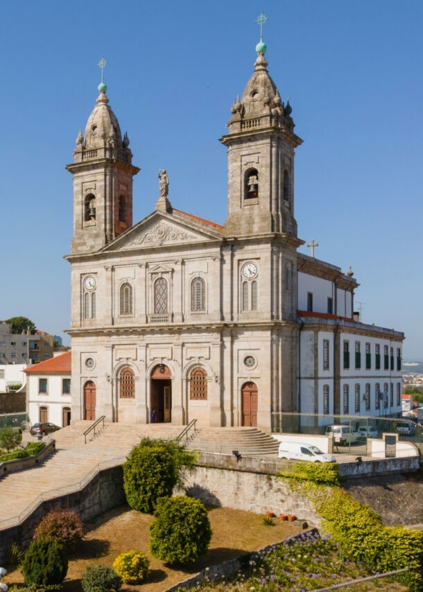 Kirche mit Zwillingstürmen auf einem Hügel über den Dächern einer südländischen Großstadt unter blauem Himmel.