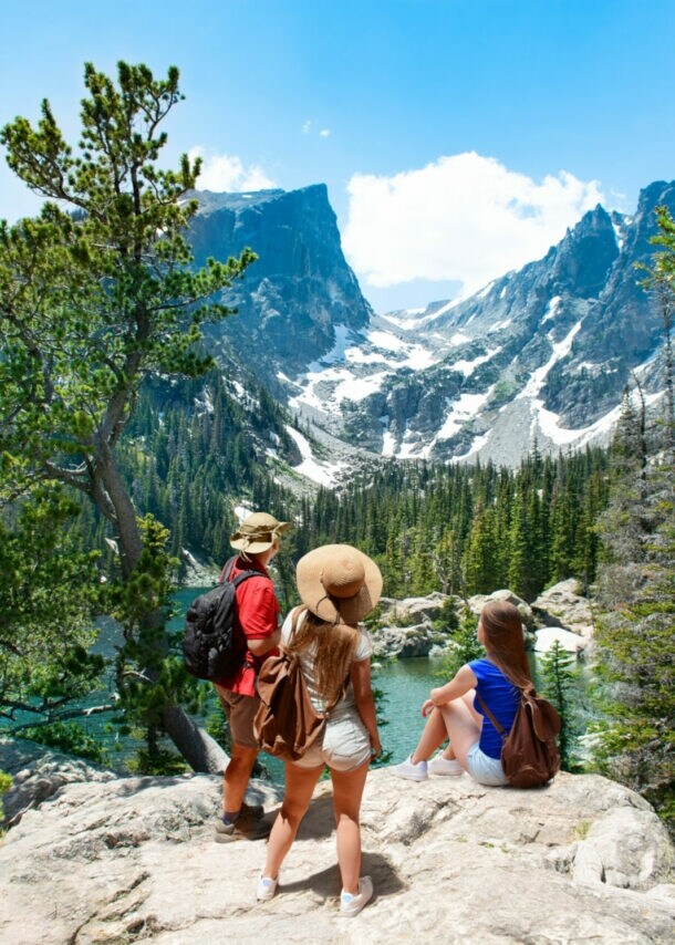 Drei Personen wandern durch die Rocky Mountains und blicken auf ein Bergpanorama.