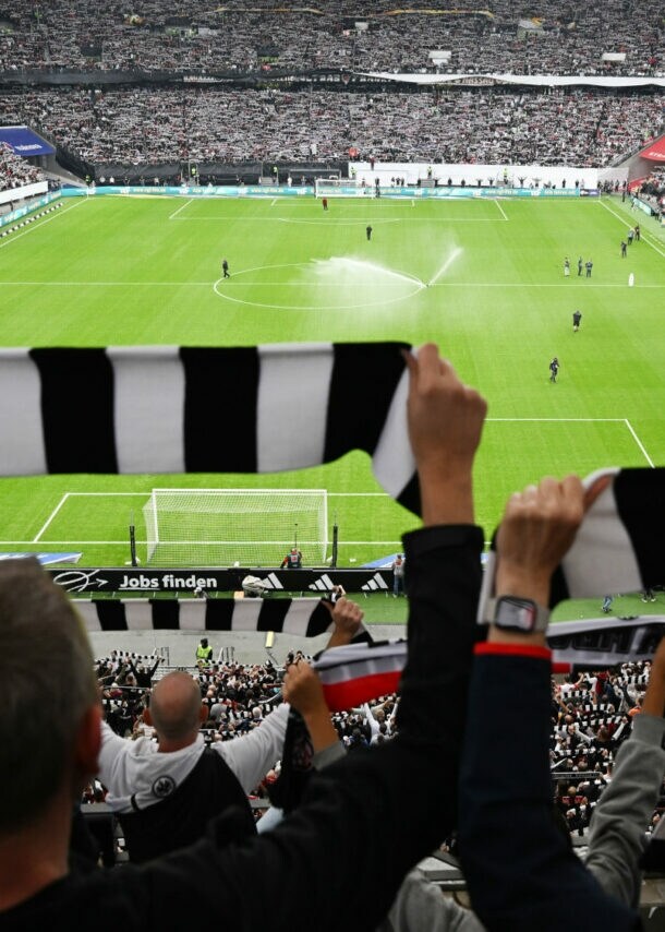 Rückansicht von Personen, die schwarz-weiß gestreifte Schals hochhalten in einem gefüllten Fußballstadion.