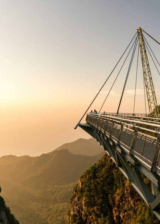 Hängende Fußgängerbrücke mit Stahlseilen über bewaldete Berge bei Sonnenuntergang auf Langkawi.