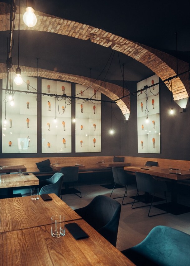 Moderner Speisesaal mit eingedeckten Holztischen und dunklen Wänden mit Gewölbedecke.