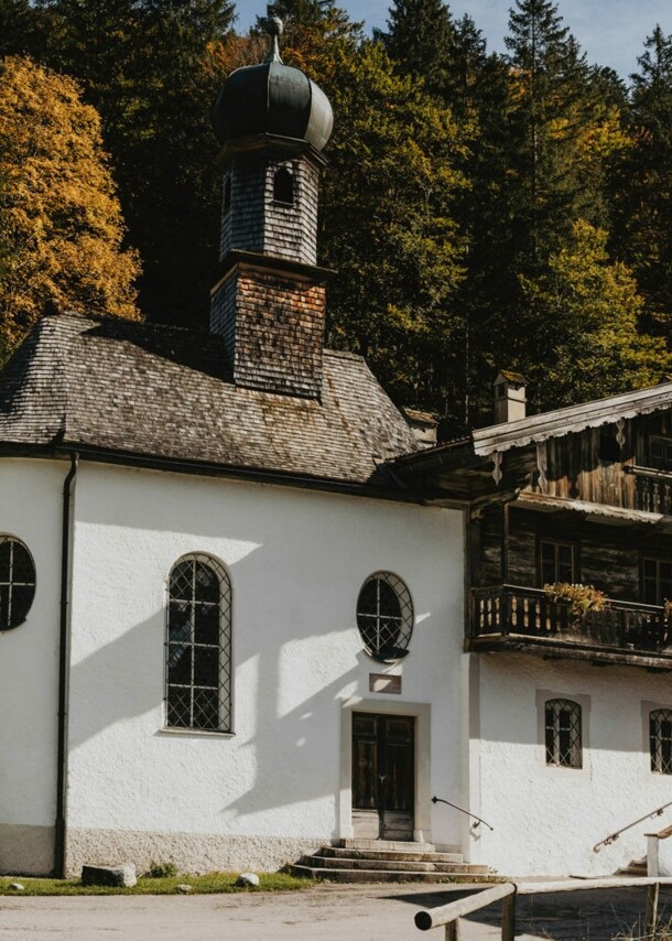 Traditionelles, bayerisches Gasthaus mit Kapelle vor einem Waldgebiet.